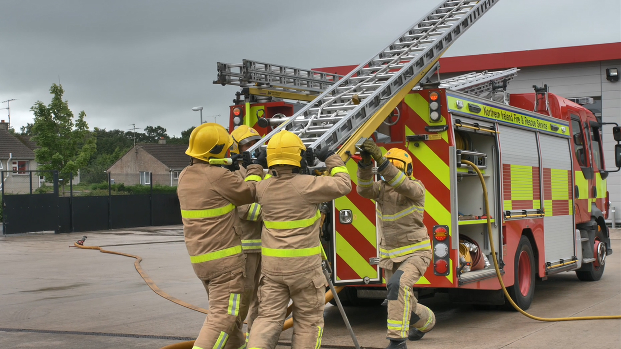 Firefighters putting ladder on fire appliance.