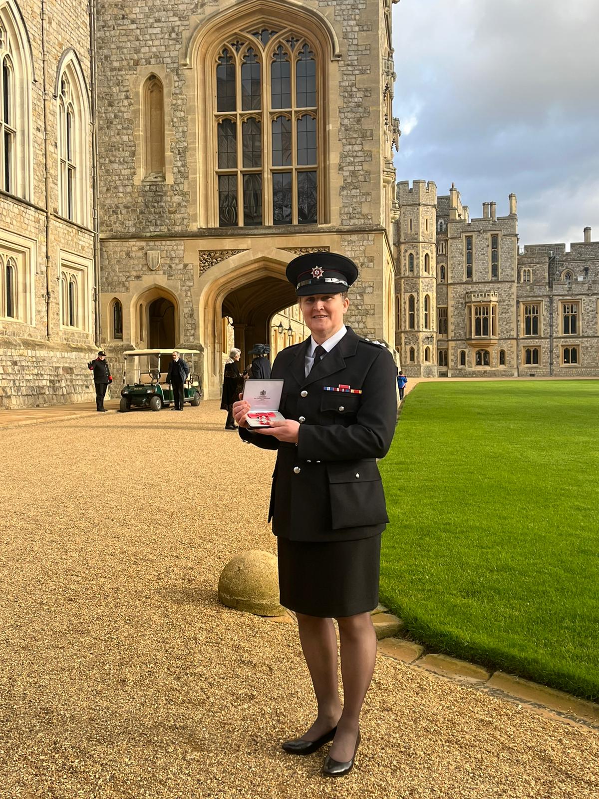 This is photography of Station Commander Karen McDowell standing while holding her MBE on a sunny day at Windsor Castle.