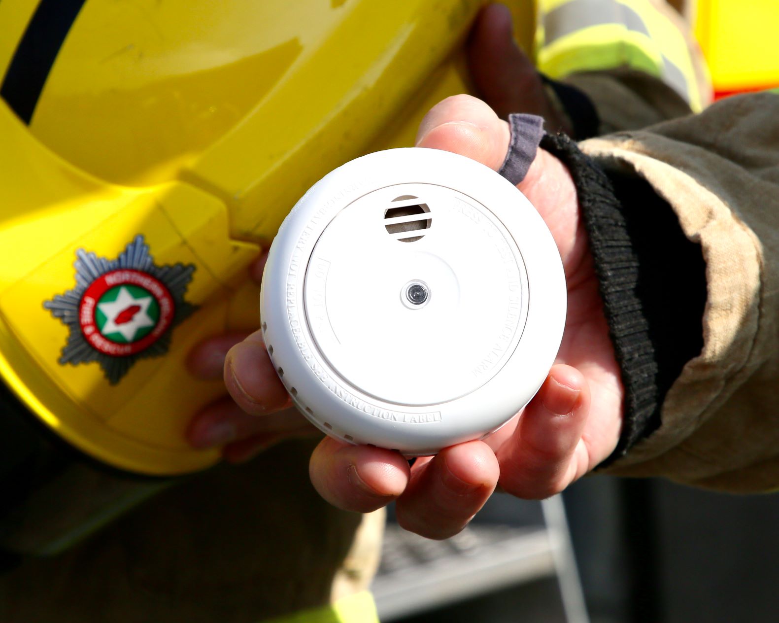 Person holding smoke alarm with Northern Ireland Fire & Rescue Service helmet.