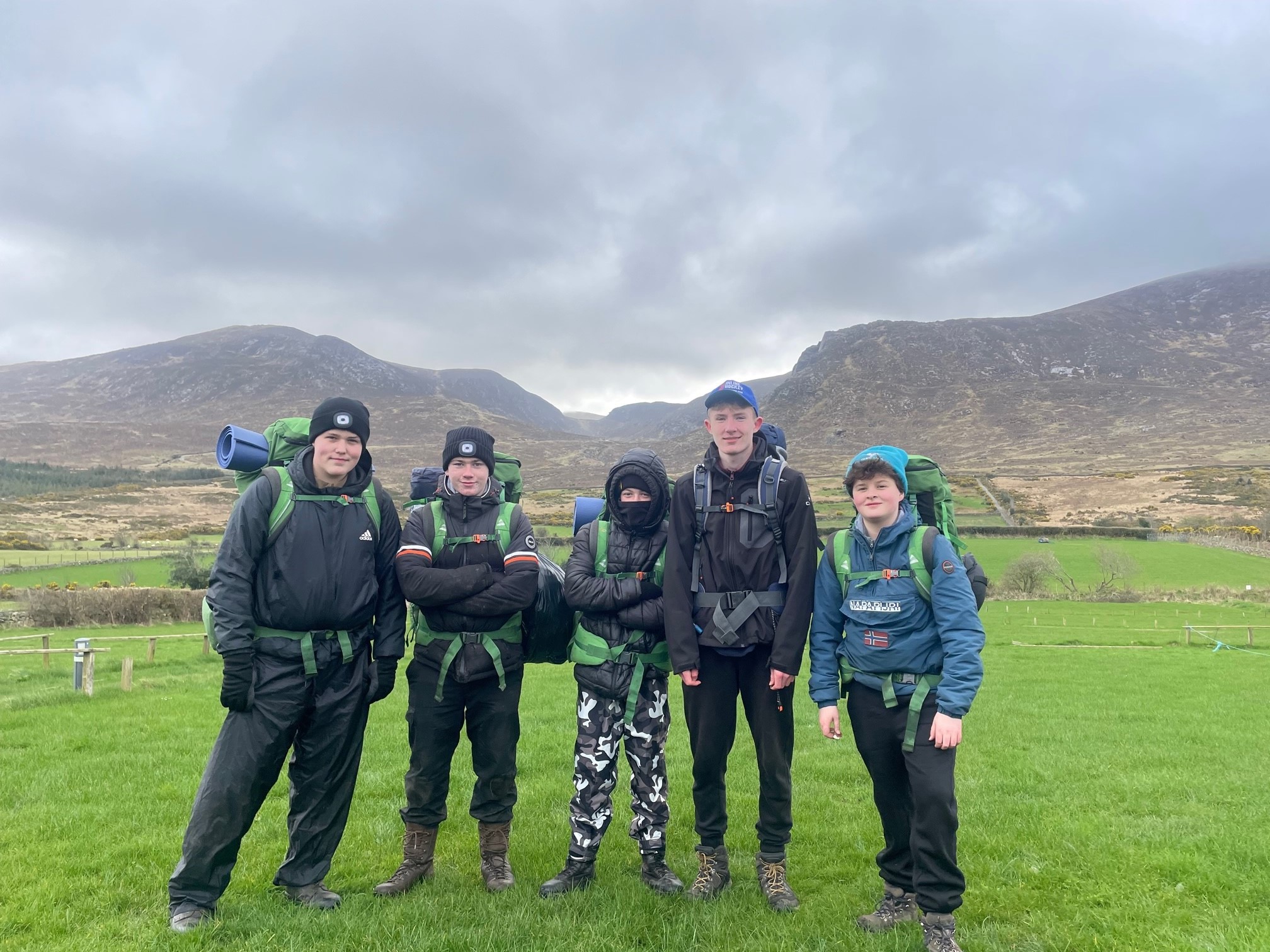 Five people standing wearing hiking clothing and backpacks with the Mourne Mountains in the background.