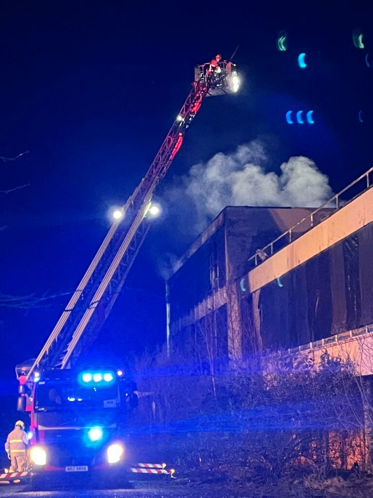 Aerial Fire Appliance beside building on fire. Firefighter standing extinguishing the fire.